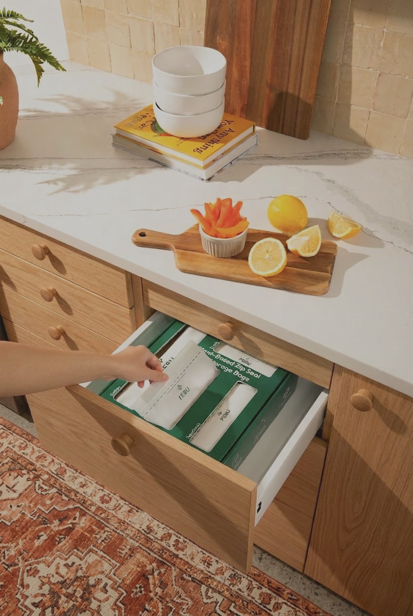 Kitchen drawer being opened with a green box inside, surrounded by fruits and books on a counter.